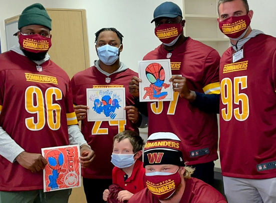 five Washington Commanders pose with a pediatric patient