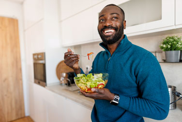 A man smiling and enjoying eating a bowl of salad