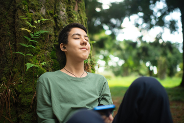 A child sitting in the park listening to music on headphones