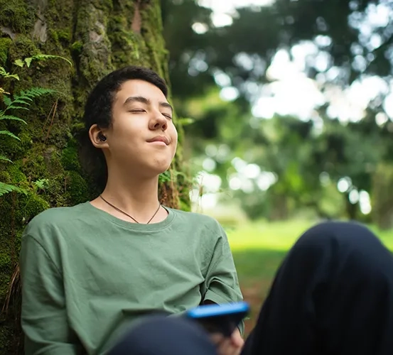 A child sitting in the park listening to music on headphones
