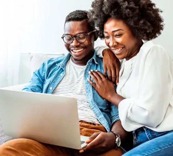 a man and woman smiling while viewing a laptop together
