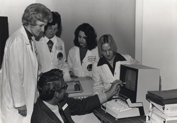 black and white photo of several nurses looking at the MIS system while a man demonstrates its use