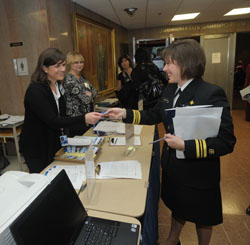 Heather Rhine hands an id badge to Leslie Wehrlen over a table in front of Masur Auditorium