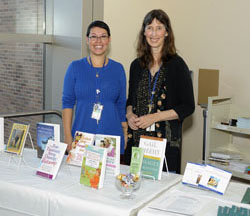 Two librarians stand in back of a table of books