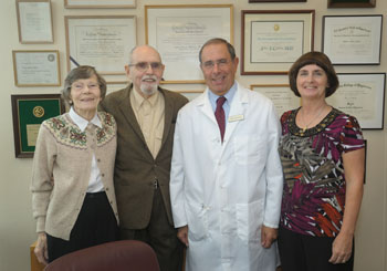 Three visitors (two women and a man) stand with Dr. John Gallin in his lab coat in his office