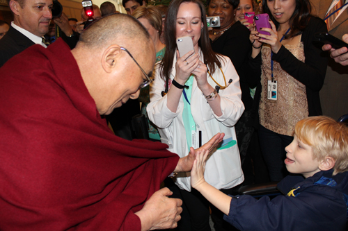 Spiritual leader, the Dalai Lama (left), and pediatric patient, Jacob Ludwig, high-five as staff watch nearby.