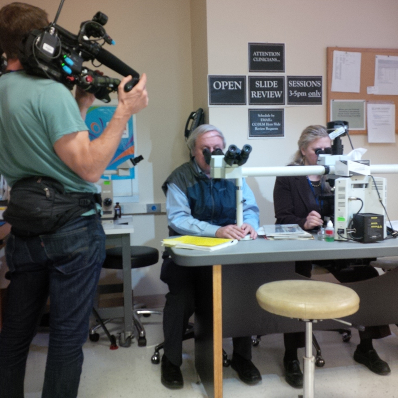Staff look through microscopes while being filmed.