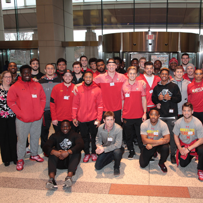 Donna Gregory, Recreational Therapy Chief, poses with football players from the University of Maryland at the Clinical Center North entrance during their visit to the NIH Clinical Center Feb. 27 to inspire patients