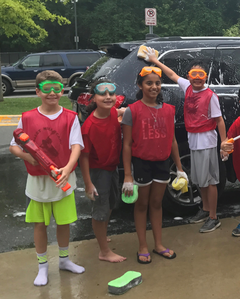 Four students with goggles and sponges wash a car. Proceeds were donated to assist NIH Clinical Center patients in need
