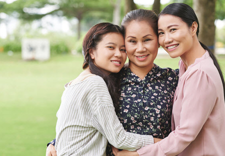 An older woman with two younger women, likely daughters, hugging her on both sides while they are outside