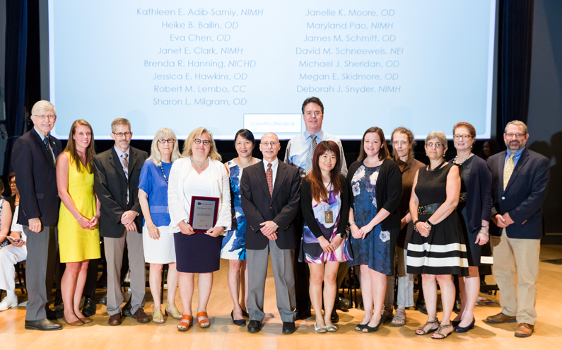 NIH Distressed Trainee Work Group award recipients on a stage. Pictured from the Clinical Center, Robert Lembo (center)
