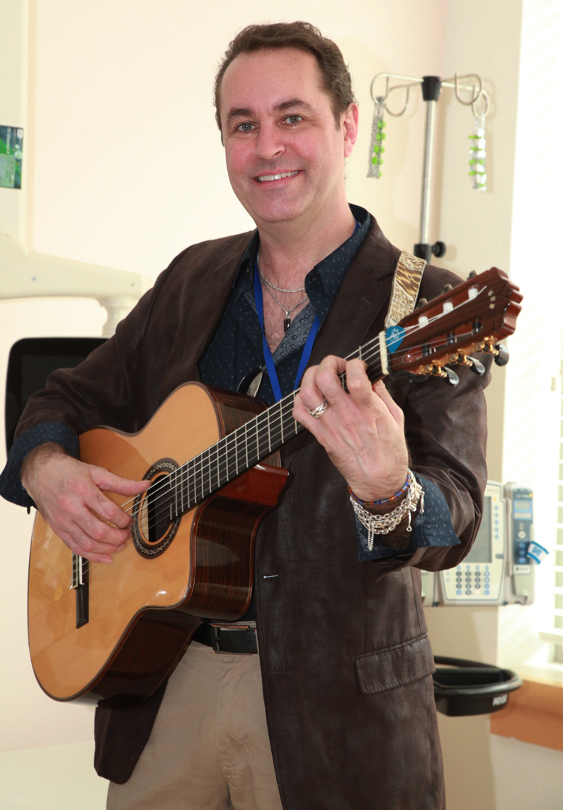 Michael Bard, a volunteer medical musician, holds his guitar in a patient room
