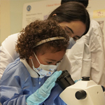 a child in a lab coat using a microscope